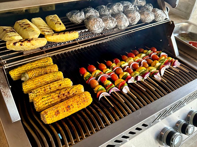 Corn, vegetable skewers and potatoes on the grill for a family-style BBQ
